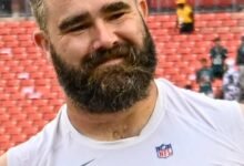 Jason Kelce smiling in a white Eagles warm-up top on the sideline
