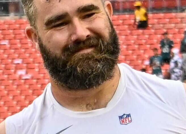 Jason Kelce smiling in a white Eagles warm-up top on the sideline